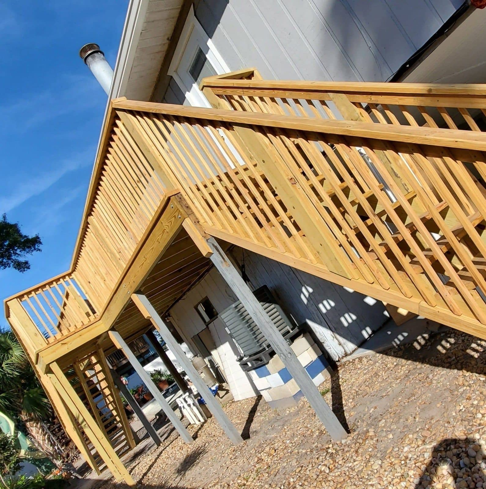 Multi-level wood deck with railings built by True Carpenters against a blue Florida sky