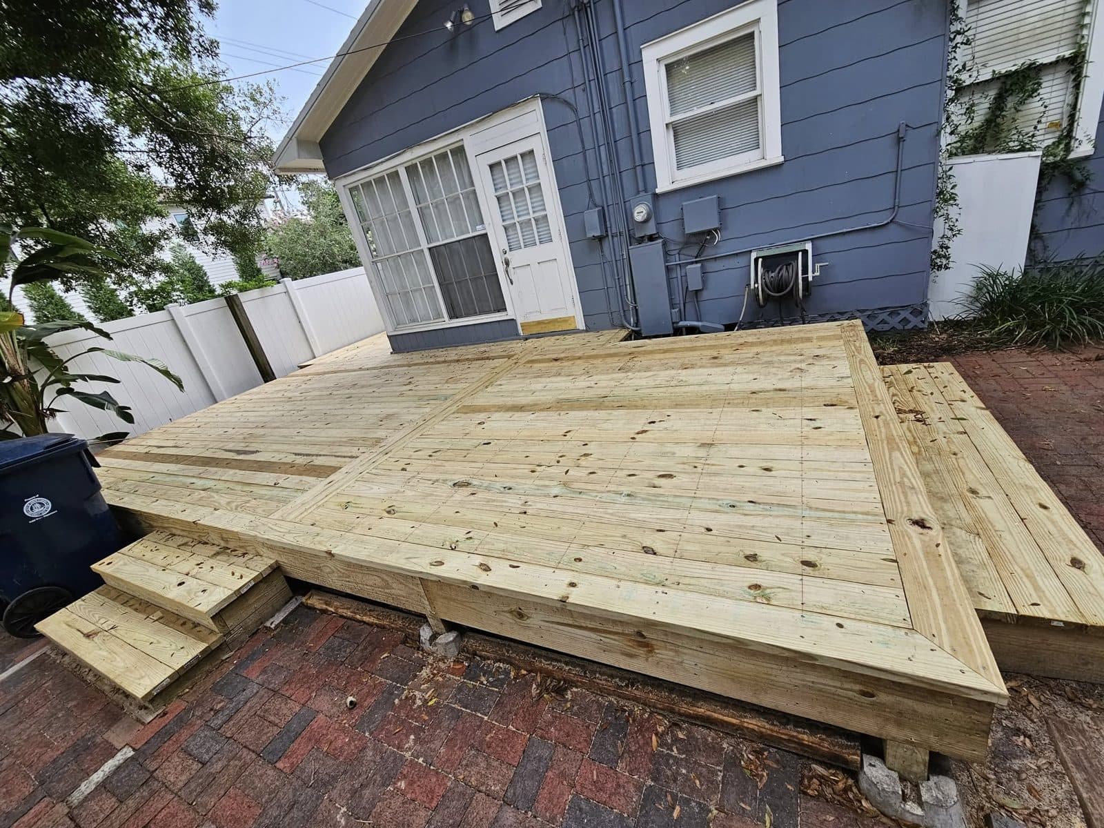 Finished ground-level backyard deck beside a blue house